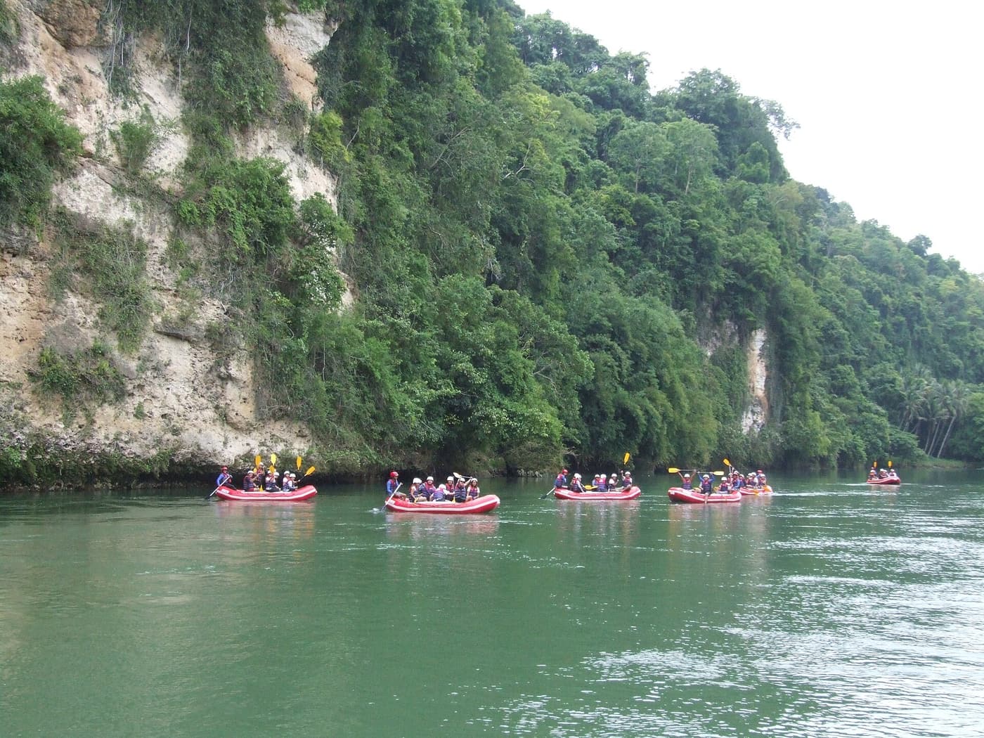 Rafts paddling down the green Cagayan de Oro River below forested cliffs