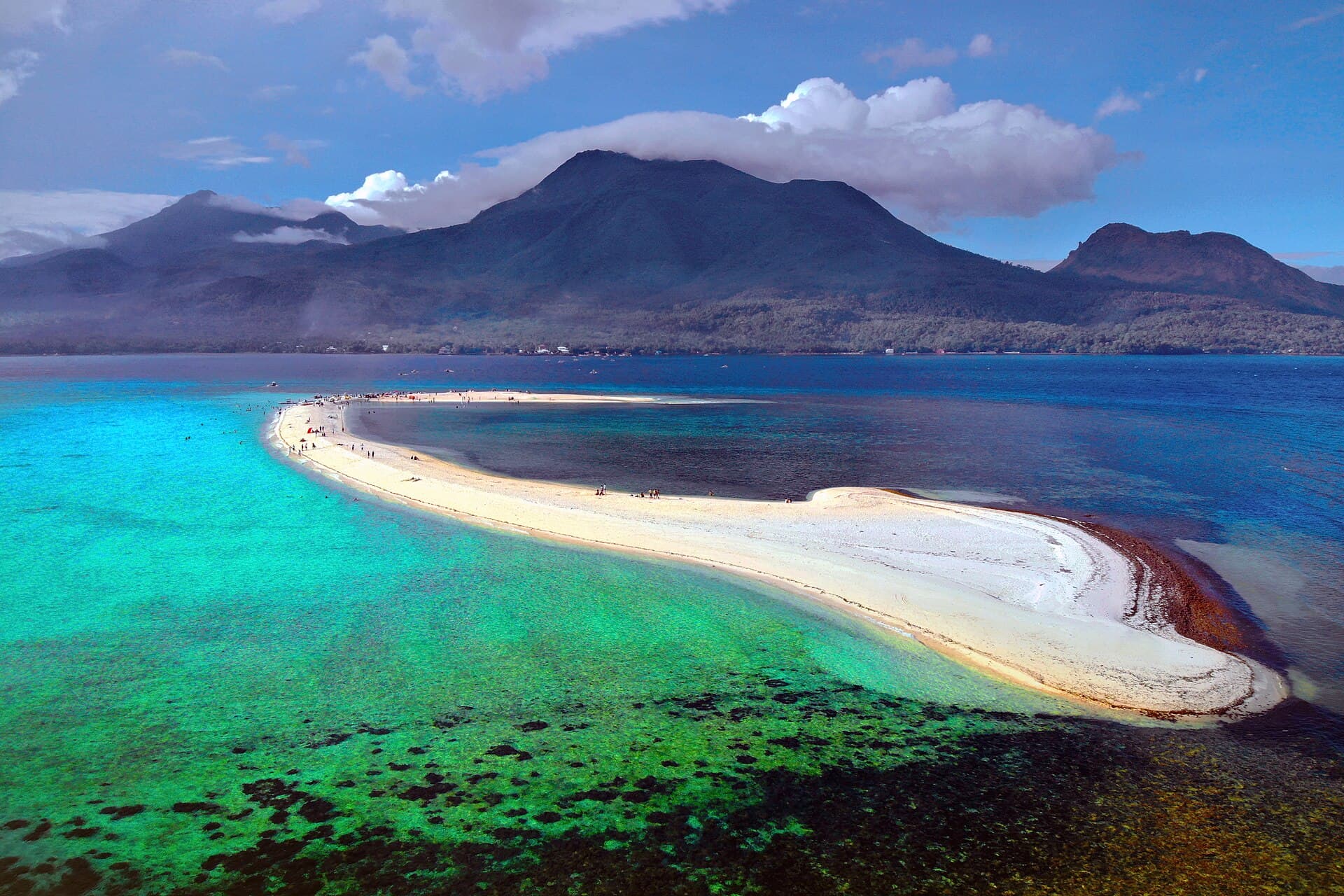 Aerial view of a curving white sandbar in turquoise water with Camiguin’s volcanoes behind